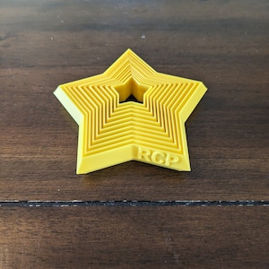 May include: A set of yellow star-shaped cookie cutters with a hole in the centre. The largest cutter has the letters "RCP" embossed on the bottom.