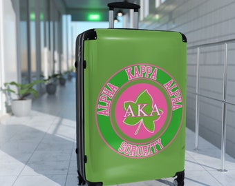 Niedlicher Alpha Kappa Sorority-Koffer – auch bekannt als rosa und grüner Soror-Reisekoffer mit griechischen Buchstaben und rundem Design.