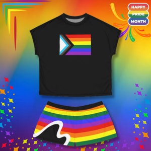 Puede incluir: Una camiseta negra de corte corto con una bandera del orgullo arcoíris y un par de pantalones cortos a juego con rayas arcoíris.