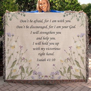 May include: A woven throw blanket with a floral design and a beige background. The blanket features a quote from the Bible, Isaiah 41:10, which reads: "Don't be afraid, for I am with you. Don't be discouraged, for I am your God. I will strengthen you and help you. I will hold you up with my victorious right hand. Isaiah 41:10"