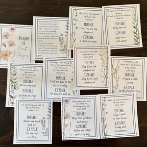 以下が含まれることがあります： 花と植物のイラストが描かれた白いカードのコレクションで、インスピレーションを与えるテキストが特徴です。各カードには白い縁取りがあり、「Inhale」や「Exhale」などのフレーズと詩篇23編からの詩が含まれています。