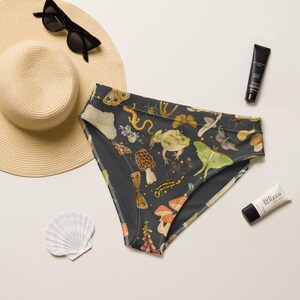 May include: High-waisted bikini bottoms in dark gray featuring a repeating pattern of frogs, moths, butterflies, mushrooms, and snails. The print includes earthy tones of green, brown, and orange. The fabric has a smooth, matte finish throughout.