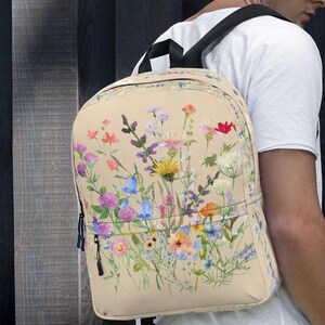 May include: A beige backpack with a floral print featuring a variety of colorful wildflowers. The backpack has black straps and zipper pulls.