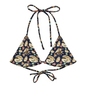 May include: A navy blue triangle bikini top with a seashell pattern. The pattern includes illustrations of seashells, pearls, and octopuses in shades of beige, orange, and teal. The top has tie closures at the neck and back.