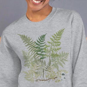 May include: A heather grey sweatshirt with a botanical print of ferns in shades of green. The ferns are arranged in a cluster and have a vintage aesthetic.