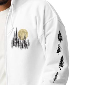 May include: White zip-up hoodie featuring a forest and moon graphic on the front and tree silhouettes on the sleeve. The design includes a yellow moon and black tree illustrations, creating a nature-inspired theme.