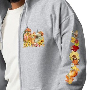 May include: A gray zip-up hoodie with a fall-themed design on the front and a vertical row of fall-themed images on the sleeve. The design on the front features pumpkins, sunflowers, and leaves. The design on the sleeve features pumpkins, sunflowers, leaves, and a mug.