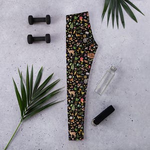 May include: Black leggings with a colorful pattern of woodland creatures, mushrooms, and plants. The pattern is repeated throughout the leggings.