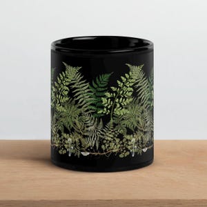 May include: Black ceramic mug with a green fern pattern. The mug has a white rim and handle.