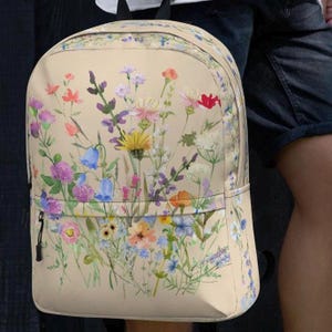 May include: A beige backpack with a floral print featuring a variety of colorful flowers, including pink, purple, blue, yellow, and red.