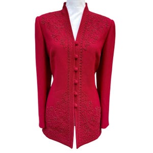 May include: A red jacket with a high collar and long sleeves. The jacket features ornate embroidered detailing with small bead accents along the front, shoulders, and hem. It has a button-up closure and a tailored fit, suitable for formal occasions.