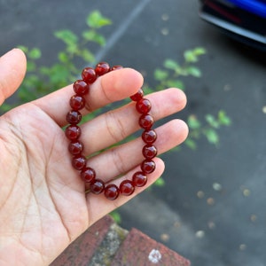 May include: A red carnelian beaded bracelet with a simple design. The bracelet is made of round beads and is strung on a clear elastic cord.