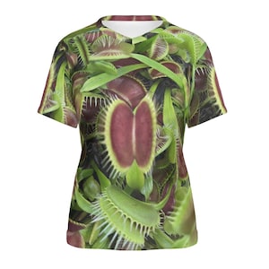 Peut inclure: Un t-shirt à manches courtes avec un imprimé vibrant de plantes de dionée attrape-mouche vertes et rouges. L'imprimé présente une vue rapprochée des pièges ouverts des plantes, révélant leurs détails complexes.