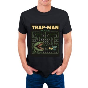 Peut inclure: T-shirt noir avec un motif de labyrinthe, une plante carnivore et une mouche. Le texte "TRAP-MAN MAZE" est imprimé en jaune au-dessus du labyrinthe. La plante carnivore a une bouche rouge et la mouche a des ailes vertes.