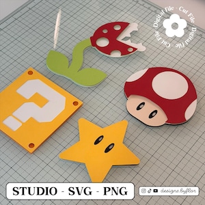 May include: A selection of colourful, die-cut paper shapes inspired by the Super Mario video game series. Includes a red and white mushroom, a yellow star, a question mark block, and a Piranha Plant. The text "STUDIO - SVG - PNG" is visible.