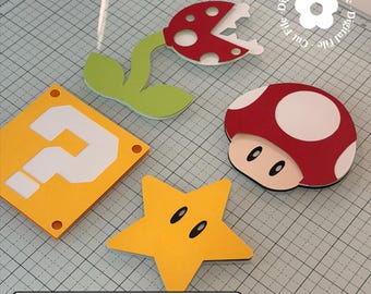 May include: A collection of colorful, die-cut paper shapes inspired by the Super Mario video game series. Includes a red and white mushroom, a yellow star, a question mark block, and a Piranha Plant. The text "STUDIO - SVG - PNG" is visible.