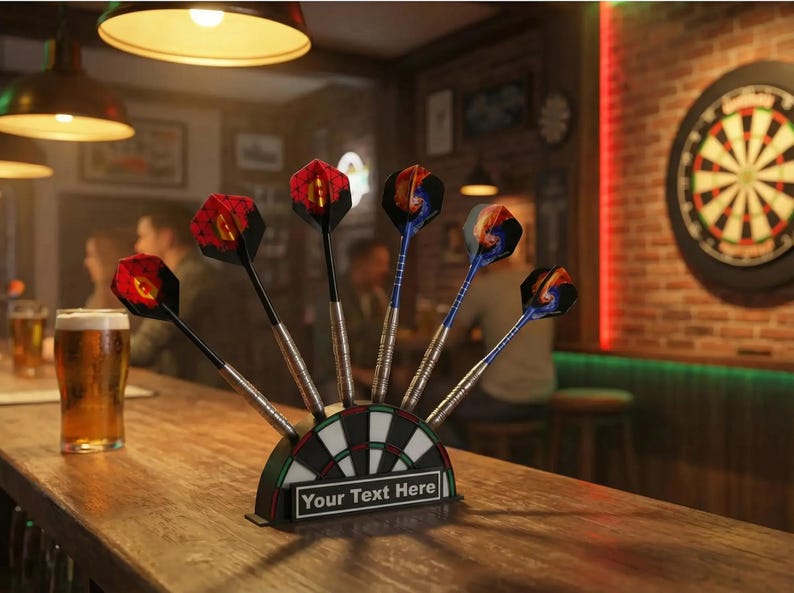 May include: A set of darts with red, black, and blue flights, displayed in a holder shaped like a dartboard. The holder has the text "Your Text Here". The scene is set in a bar with a dartboard in the background.