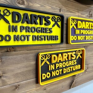 May include: Three yellow and black signs with the text "DARTS IN PROGRES DO NOT DISTURB" and a crossed darts graphic. One sign is purple and black.