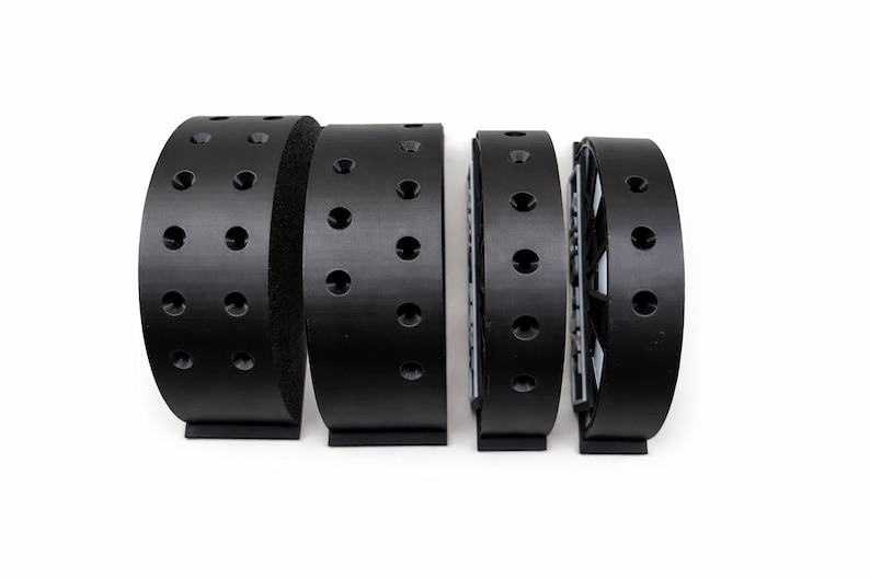 May include: Four black curved objects with evenly spaced holes, possibly parts of a larger mechanism, are arranged in a row against a white background. The objects have a matte finish and a rectangular base.