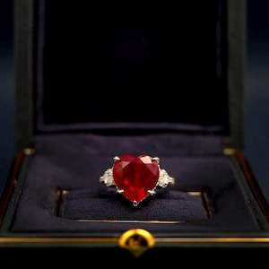 Puede incluir: Un anillo de rubí en forma de corazón engastado en oro blanco con diamantes más pequeños en la banda.