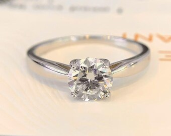 May include: A silver solitaire engagement ring with a round brilliant cut diamond.
