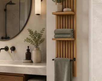 May include: A vertical wall-mounted wooden shelf unit featuring a slatted back panel, two horizontal shelves, and a black metal towel bar. The shelves hold a small potted plant and a decorative bowl, while folded gray towels rest on a shelf.