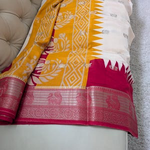 K&ouml;nnte beinhalten: Ein lebendiges Textil mit Gelb, Wei&szlig; und Fuchsia. Der Stoff zeigt komplizierte Muster, darunter geometrische Formen und florale Motive. Der Rand ist mit einem detaillierten Design verziert, was die Gesamt&auml;sthetik erh&ouml;ht.