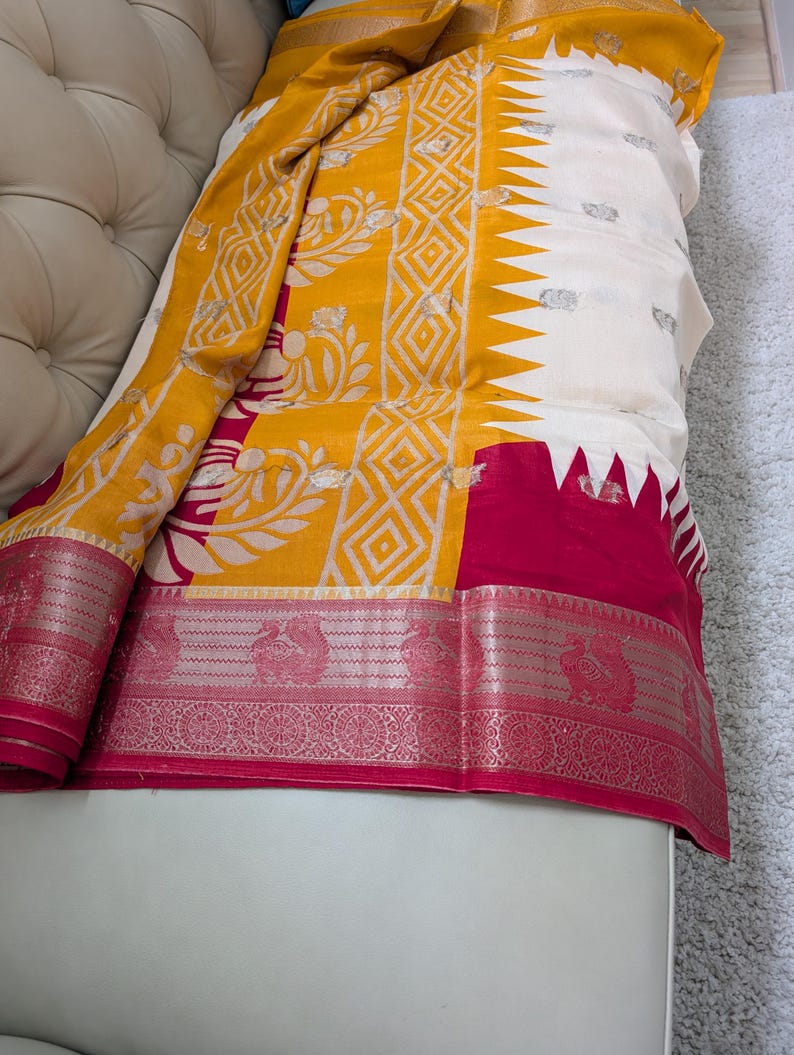 K&ouml;nnte beinhalten: Ein lebendiges Textil mit Gelb, Wei&szlig; und Fuchsia. Der Stoff zeigt komplizierte Muster, darunter geometrische Formen und florale Motive. Der Rand ist mit einem detaillierten Design verziert, was die Gesamt&auml;sthetik erh&ouml;ht.