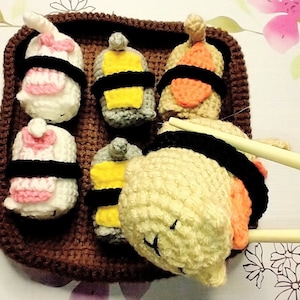 May include: A crocheted sushi set with a variety of fillings, including salmon, tuna, and cucumber. The sushi is arranged on a brown crocheted tray and is being picked up with chopsticks.