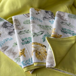 May include: Five white fabric burp cloths with a jungle animal print. The cloths have a yellow backing.