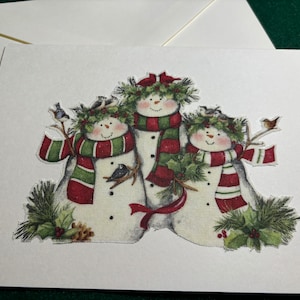 Cartes de Noël fabriquées à la main. Bonhommes de neige en tissu coupés à la main avec cardinaux, écharpes, mésanges et autres oiseaux, feuilles et baies de houx, et pin.