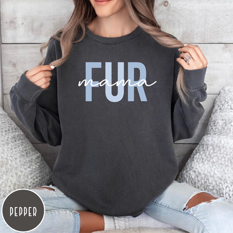 May include: A dark gray sweatshirt with the text "FUR mama" in light blue letters. The sweatshirt is being worn by a person.