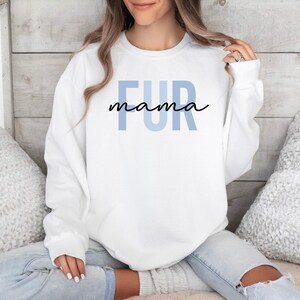 May include: White sweatshirt with the text "FUR mama" in blue and black lettering.