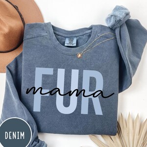 May include: A blue denim sweatshirt with the text "FUR mama" in white and black lettering. The sweatshirt is a comfortable, casual style.