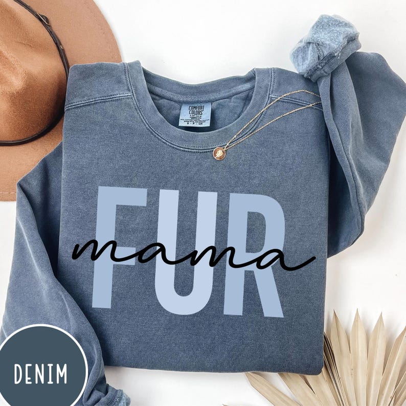 May include: A blue denim sweatshirt with the text "FUR mama" in white and black lettering. The sweatshirt is a comfortable, casual style.
