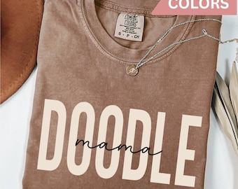 May include: A brown t-shirt with the text "DOODLE mama" in white with a black outline. The shirt is made by Comfort Colors and is in the color Espresso.