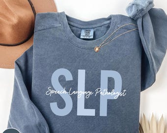 May include: A blue denim sweatshirt with the text "SLP Speech-Language Pathologist" in white lettering. The sweatshirt has a distressed look and is a comfortable, casual style.
