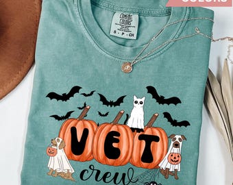 Peut inclure: Un t-shirt bleu sarcelle avec un motif sur le thème d'Halloween représentant des citrouilles, des chauves-souris, un chat et deux chiens. Les citrouilles épellent "VET" et le texte "crew" est en dessous. Le t-shirt porte une étiquette indiquant "Comfort Colors".