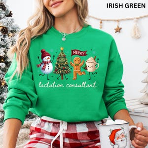 May include: An Irish green long-sleeve sweatshirt featuring a graphic of a snowman, a Christmas tree, a gingerbread person holding a banner that says MERRY, and a mug of cocoa. The text lactation consultant is printed below the graphic.