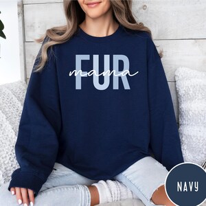 May include: A navy blue sweatshirt with the text "FUR mama" in light blue letters. The sweatshirt is shown on a model wearing light blue jeans.