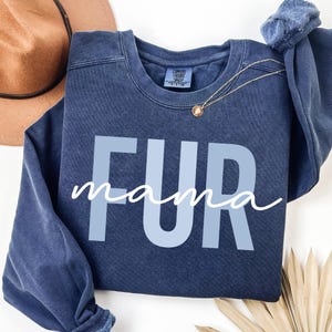 May include: A dark blue sweatshirt with the text "FUR mama" in light blue letters. The sweatshirt has a distressed look and is made of a soft, comfortable fabric.