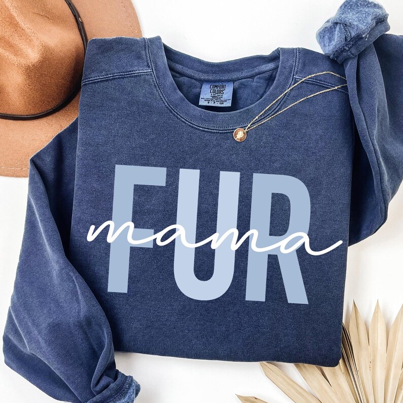 May include: A dark blue sweatshirt with the text "FUR mama" in light blue letters. The sweatshirt has a distressed look and is made of a soft, comfortable fabric.