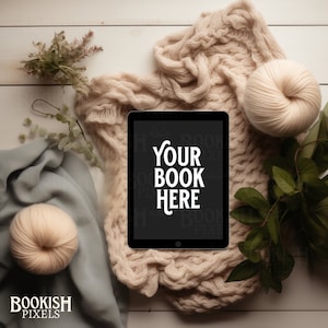 Op de afbeelding: Een zwarte tablet met de tekst "YOUR BOOK HERE" ligt op een crèmekleurige gebreide deken. Een bol wol, een grijze sjaal en groen omringen de tablet. Het Bookish Pixels-logo staat linksonder.