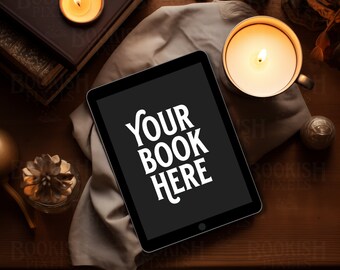 May include: A black tablet computer with a white screen displaying the text "YOUR BOOK HERE" on a wooden table with candles and books.