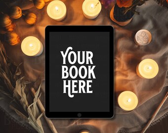 May include: A black tablet with the text "YOUR BOOK HERE" displayed on the screen. The tablet is surrounded by lit candles and dried flowers on a brown fabric surface.
