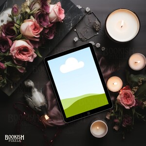 May include: A tablet computer with a green and blue landscape screen saver on a dark surface with candles, flowers, and other decorative items.