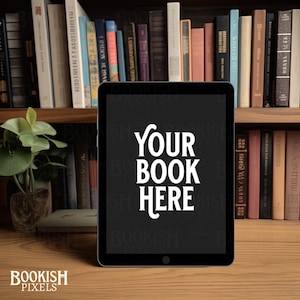 May include: A black tablet computer with a blank screen displaying the text "YOUR BOOK HERE" in white. The tablet is sitting on a wooden surface in front of a bookshelf filled with books.
