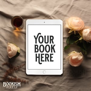 May include: A white tablet computer with a white background and the text "YOUR BOOK HERE" displayed on the screen. The tablet is surrounded by pink roses and a glass of amber liquid on a beige fabric surface.