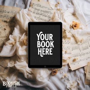 May include: A black tablet computer with a white background. The screen displays the text "YOUR BOOK HERE". The tablet is surrounded by white fabric, sheet music, and dried flowers.