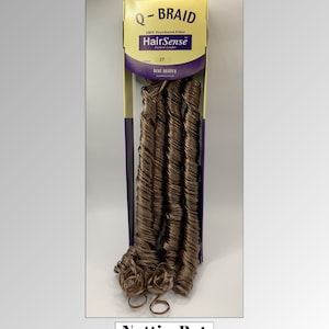 May include: Q-BRAID hair extensions in color 27. The package features the HairSense brand and the text "100% Toyokalon Fiber". The extensions are a light brown color and have a curly texture. The bottom of the package has the text "Nuttin But Wigs Hair Extensions".